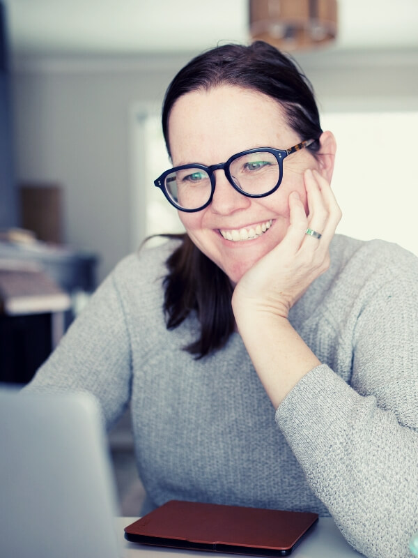 Mujer trabajando con su laptop, con lentes y sonriendo. Foto tamaño vertical