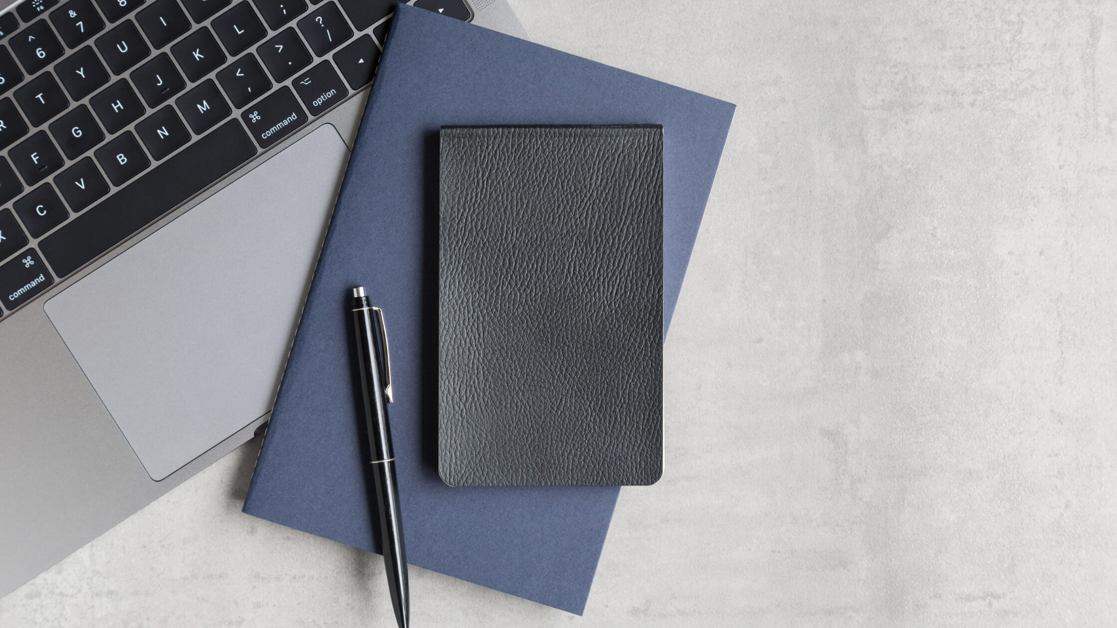 Laptop moderna con libreta negra elegante y bolígrafo sobre una mesa, simbolizando la preparación para una sesión de trabajo productiva o una reunión de negocios